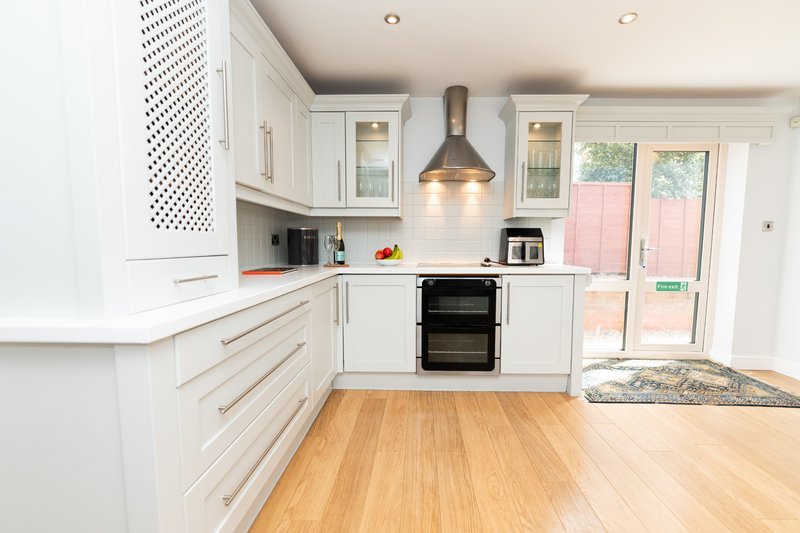 Modern white kitchen with wooden flooring, black oven, and glass doors to garden