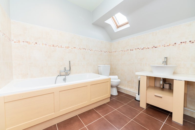 Spacious bathroom with wooden vanity, bathtub, toilet, sink, skylight and terracotta floor tiles
