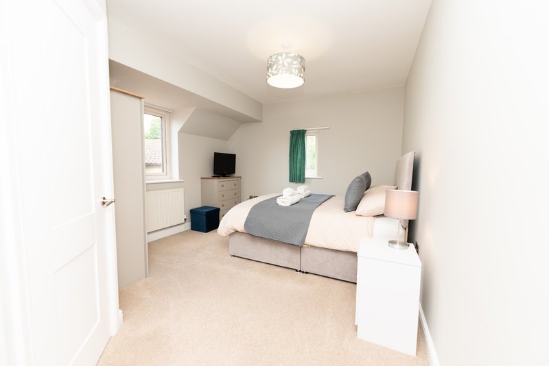 Bright bedroom with double bed, grey bedding, white furniture, TV, and carpeted floor