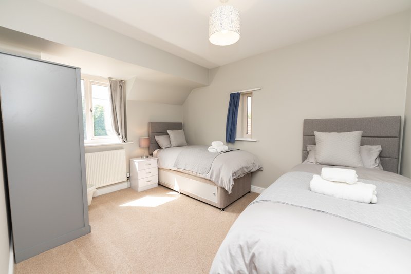 Bright attic bedroom with two single beds, grey headboards, white bedding and carpet flooring