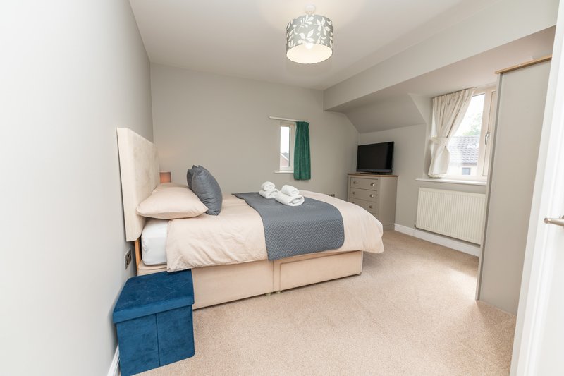 Bright bedroom with double bed, grey throw, blue towel, TV and windows with curtains
