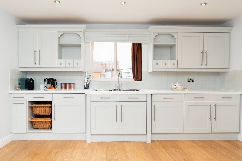 Modern white kitchen with integrated appliances, wooden worktops, and window overlooking garden