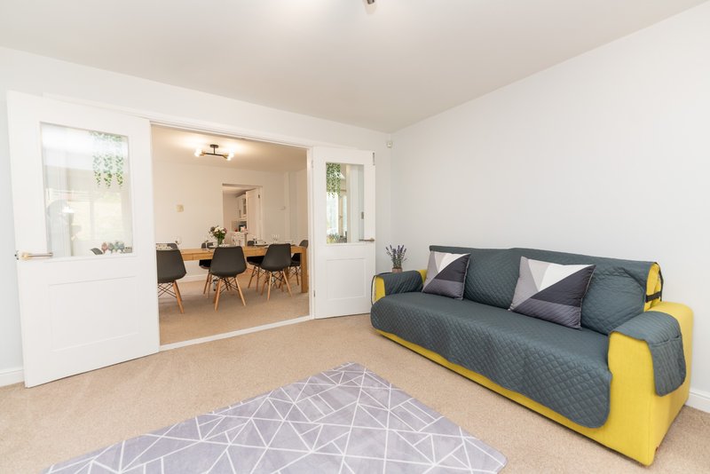 Open-plan living area with grey and yellow sofa, geometric rug, and dining space visible through open doorway