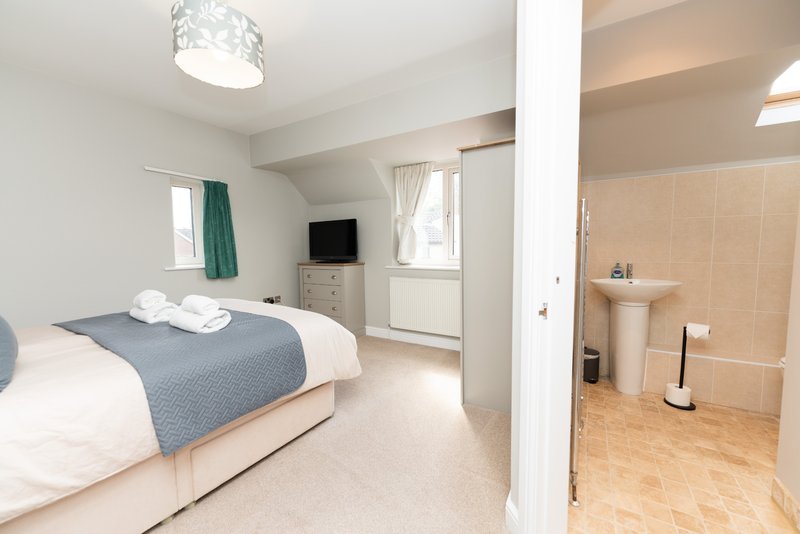 Bright bedroom with double bed, gray throw, small TV, and ensuite bathroom visible