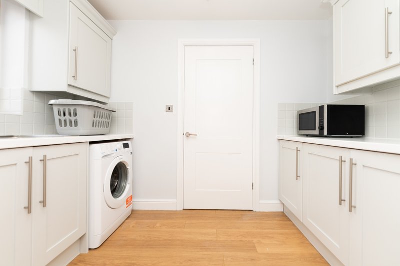 Modern white kitchen with washing machine, microwave, wooden flooring and white door