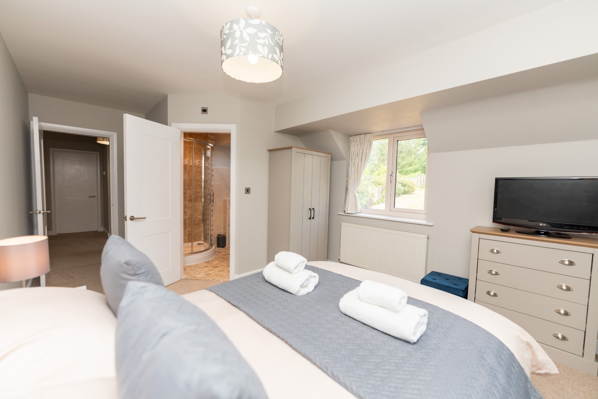 Modern bedroom with twin beds, dresser, flat-screen TV, ensuite bathroom and window