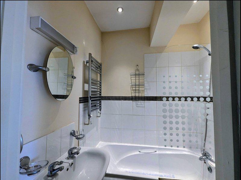 Modern bathroom with white tiles, towel rail, mirror, sink and bathtub with shower screen