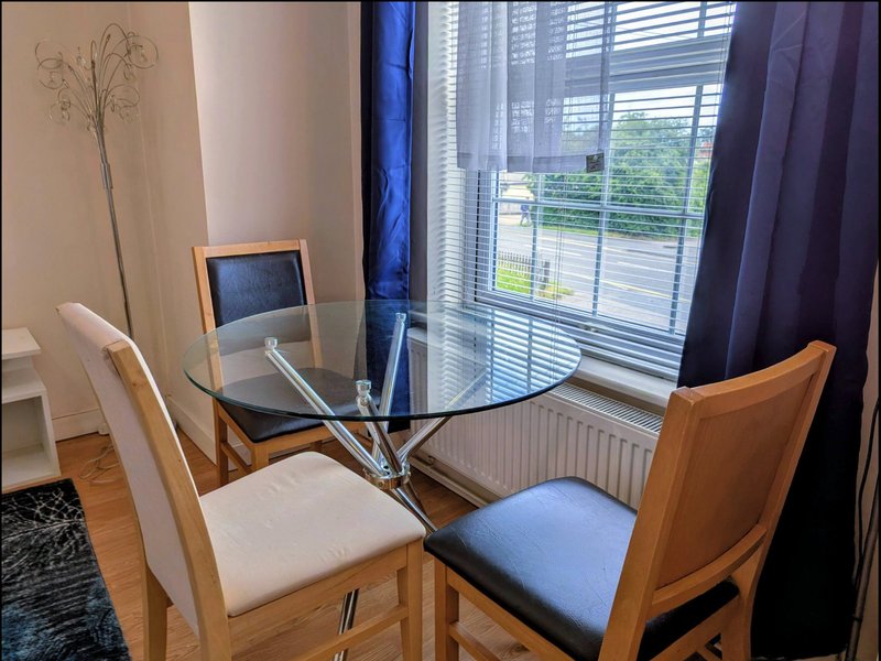 Dining area with glass table, wooden chairs, and large windows with blue curtains