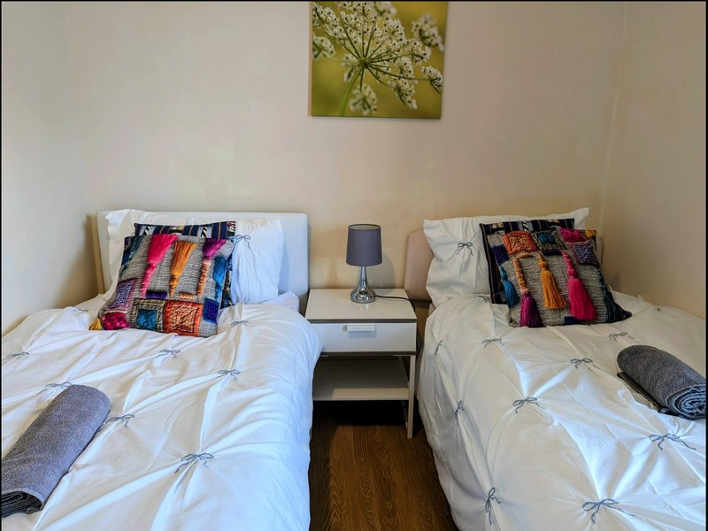 Twin bedroom with white bedding, colorful patterned pillows, bedside table and wall art