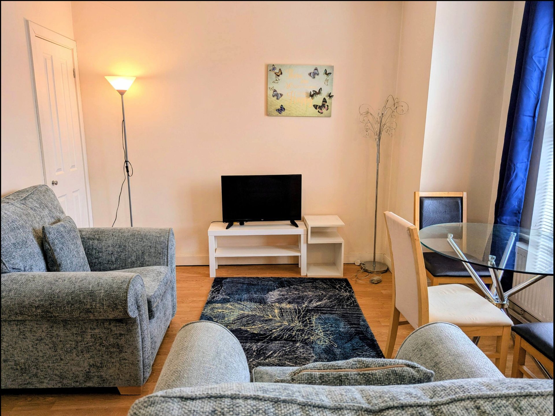 Living room with grey armchairs, TV on white stand, floor lamp and wall art