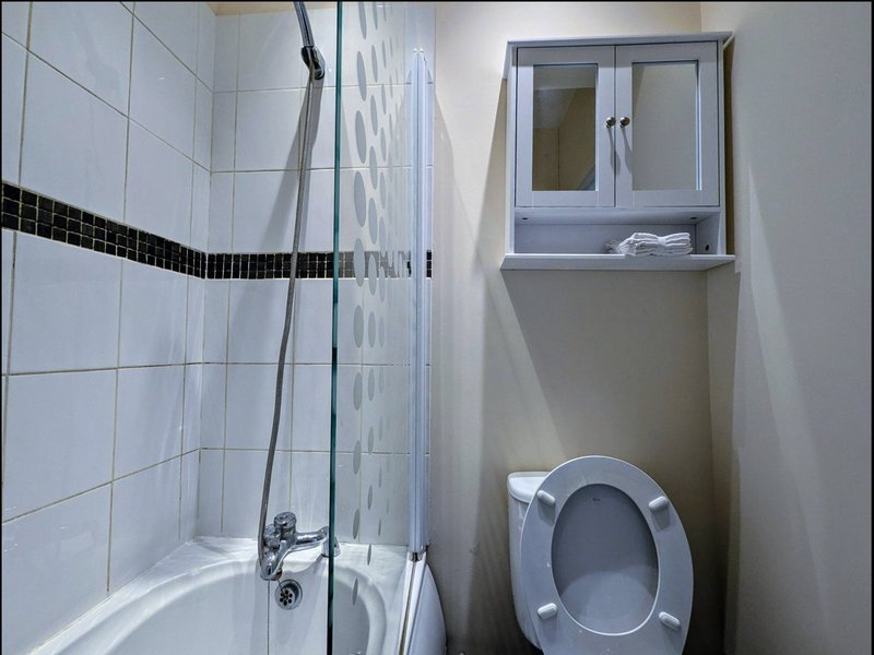 Bathroom with white tile walls, shower cubicle, toilet, and wall-mounted storage cabinet