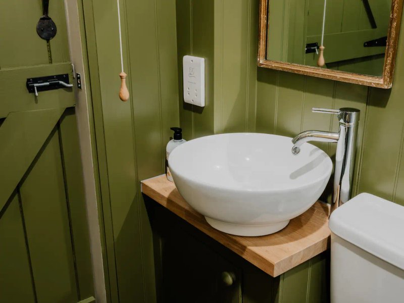 Green bathroom with white bowl sink on wooden countertop and mirror