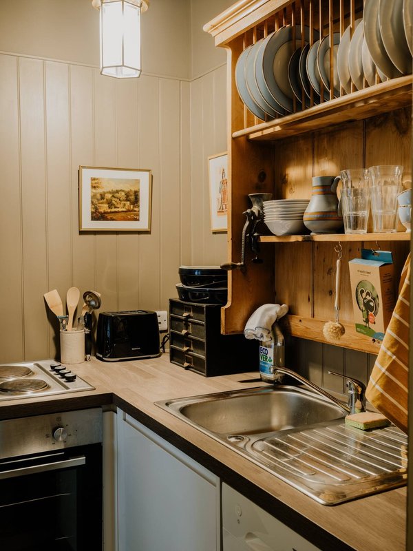 Compact kitchen with wooden open shelving, stainless steel sink, cream walls and pendant lighting