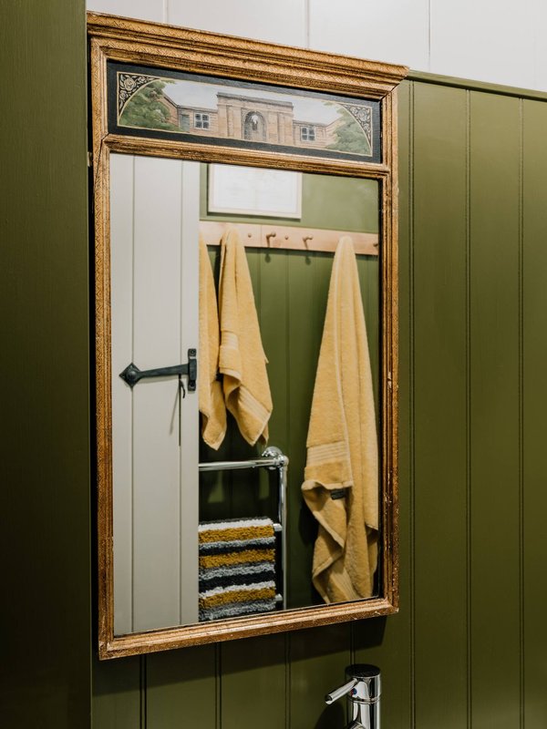 Bathroom mirror with gold frame, yellow towels and stacked towels on shelf below