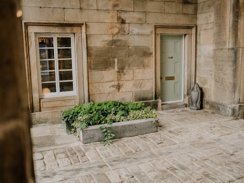 Stone courtyard with planted planter box, wooden-framed window and pale green door
