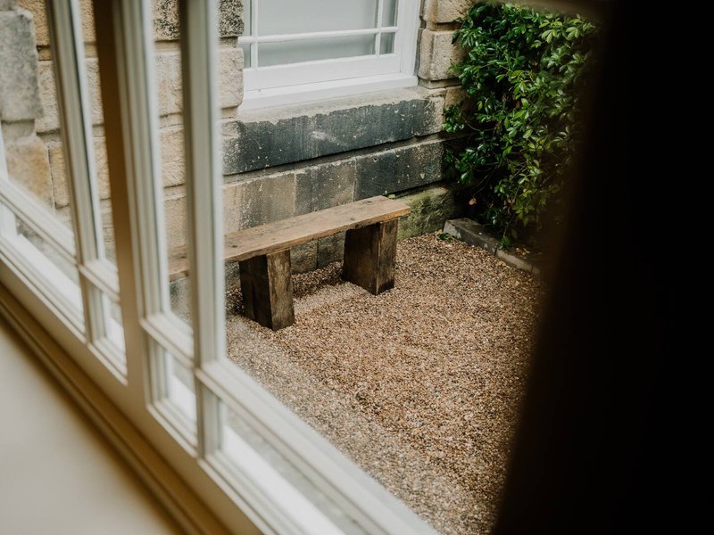 View through glass door to patio with wooden bench and ivy-covered wall