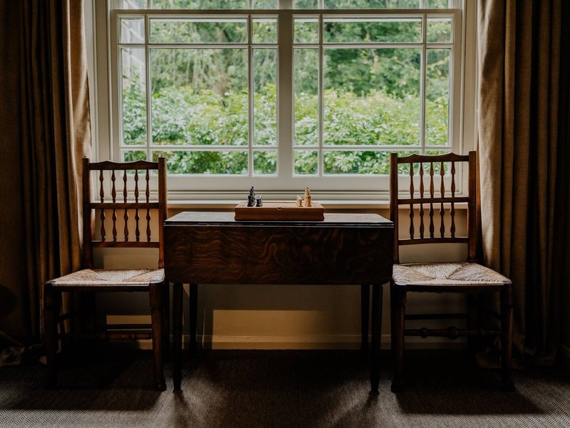 Dark wooden piano with two chairs positioned by large bay window overlooking garden