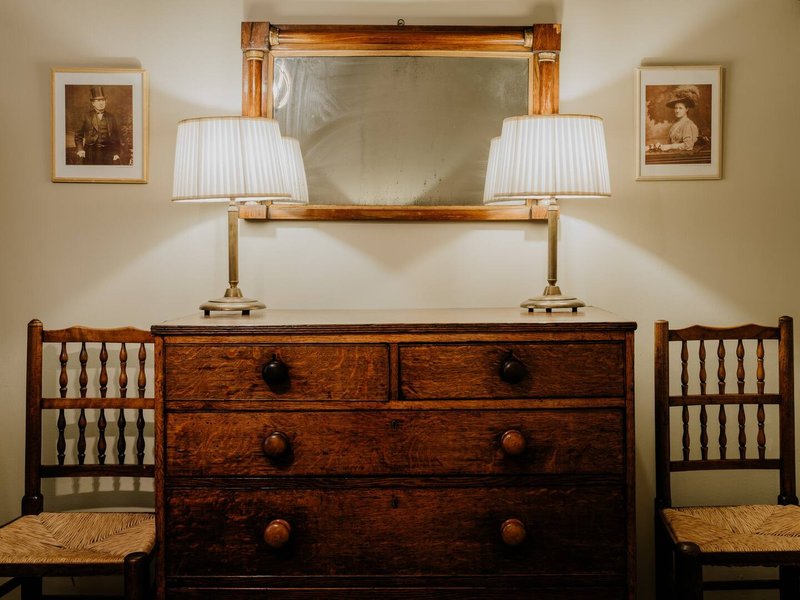 Bedroom dresser with mirror, lamps, framed artwork and wooden chairs
