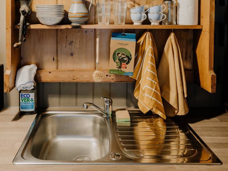 Compact kitchen sink with stainless steel basin, wooden shelving above with dishes, cups, and storage containers