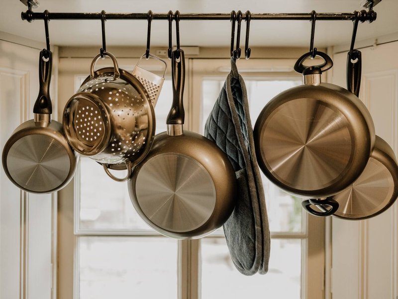 Kitchen cookware hanging from rod above window, including pans, strainers and cloth