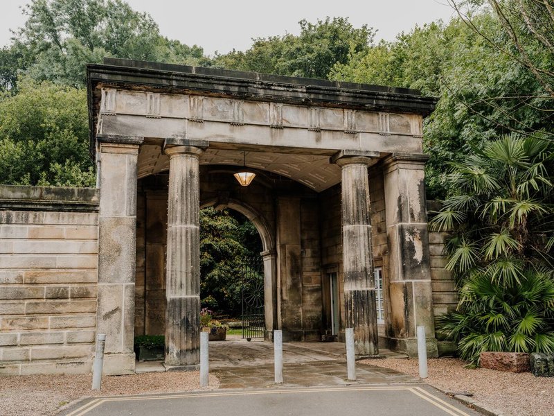 Classical stone gateway with columns and archway surrounded by mature trees and greenery