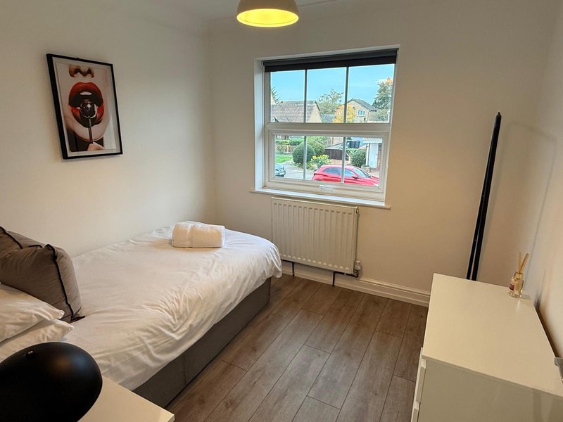 Bedroom with single bed, white desk, framed wall art, and window with street view