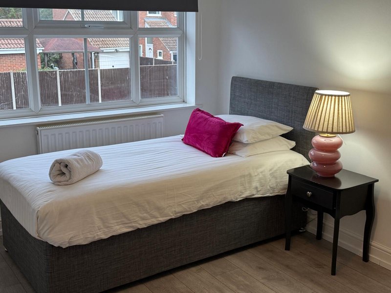 Bedroom with double bed, pink cushion, bedside lamp and large window overlooking street