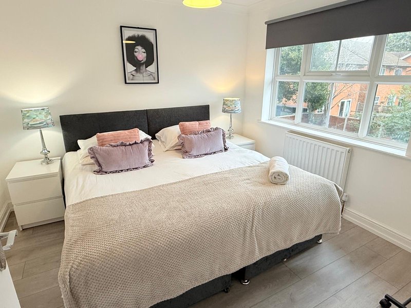 Bright bedroom with double bed, black headboard, pink cushions and large window overlooking garden
