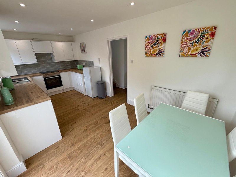 Modern kitchen and dining area with white cabinetry, wooden flooring, mint green table and colorful wall art