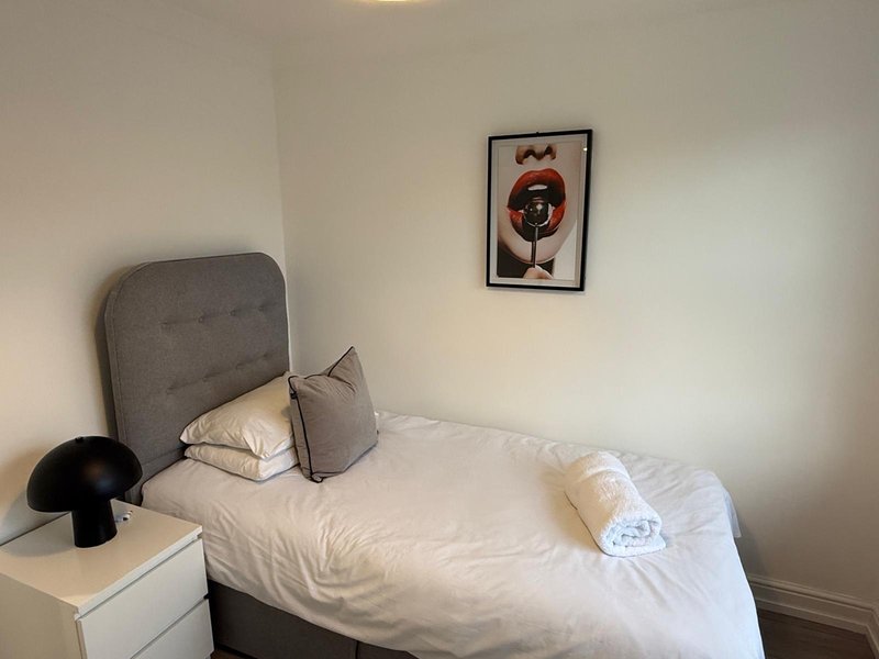 Small bedroom with single bed, grey headboard, white bedding, and minimalist wall art