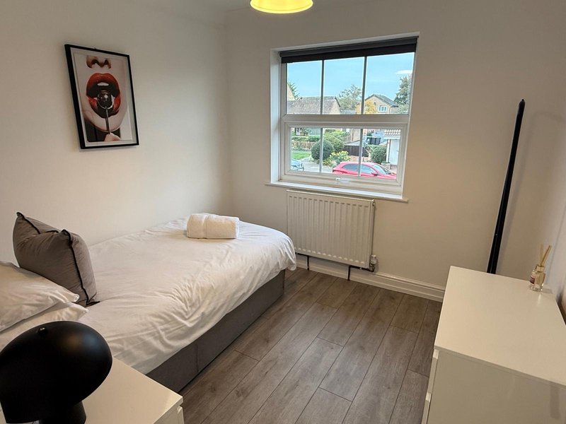 Bedroom with single bed, white bedding, wooden floor, window and wall art