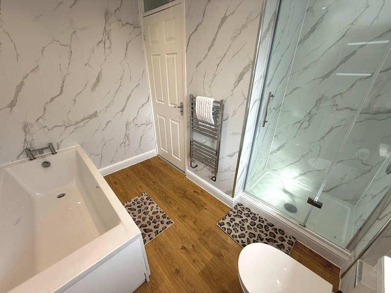 Modern bathroom with marble-effect walls, wooden flooring, white suite and glass shower enclosure