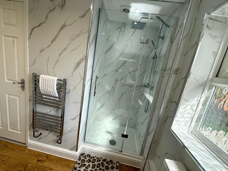 Modern bathroom with marble-effect wall tiles, walk-in shower enclosure, heated towel rack and window