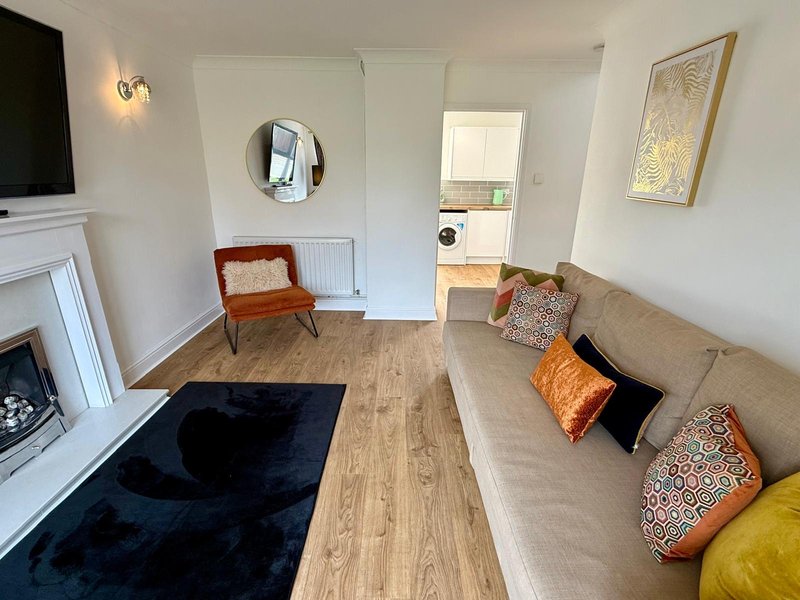 Bright living room with sofa, fireplace, wooden flooring, and access to kitchen