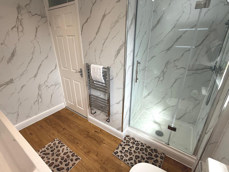 Modern bathroom with marble-effect tiles, wooden flooring, glass shower enclosure and towel rail