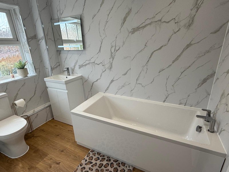 Modern bathroom with white suite, marble-effect wall tiles, wooden floor and window