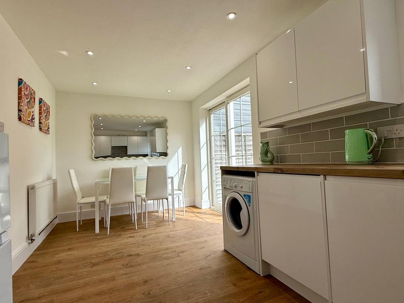 Modern kitchen with white cabinetry, green backsplash, wooden countertop and dining area with mirror