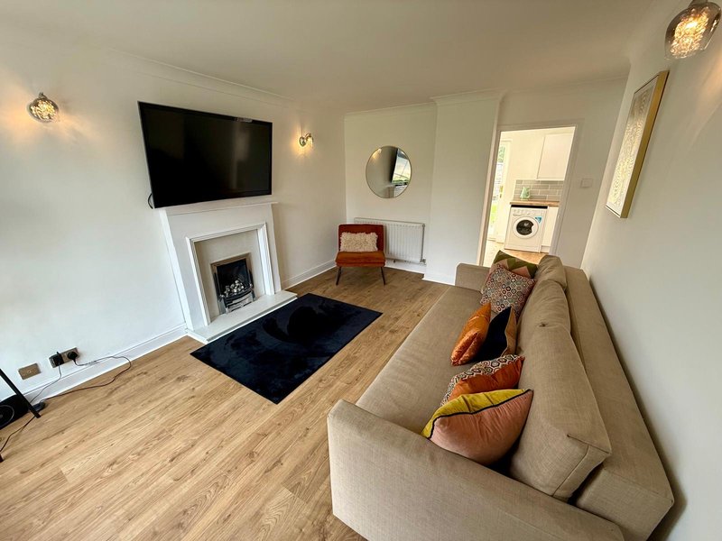 Modern living room with beige sofa, wall-mounted TV, fireplace, and wooden flooring