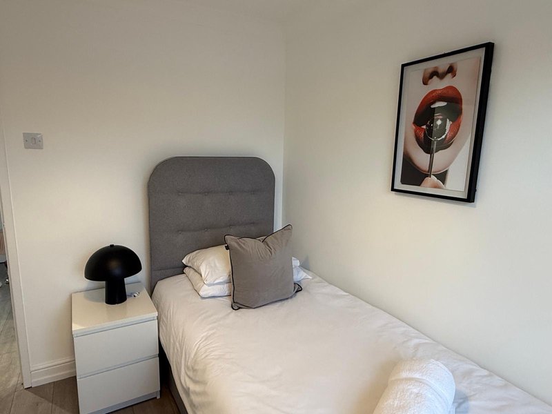Bedroom with single bed, grey upholstered headboard, white bedding, and wall art