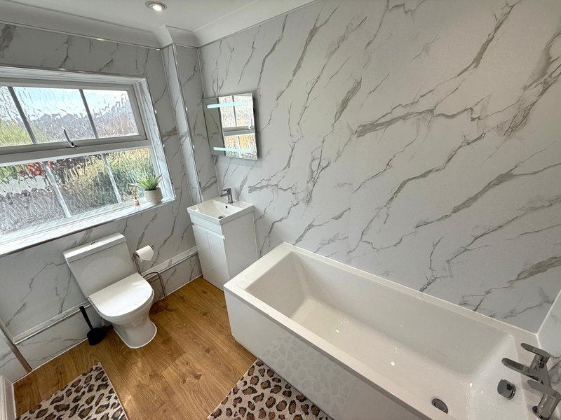 Modern bathroom with marble-effect walls, freestanding bathtub, toilet, and window with garden view