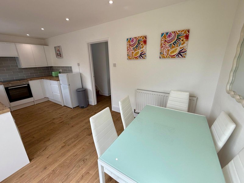 Open-plan kitchen and dining area with white cabinetry, wooden flooring, mint-green table and colorful wall art