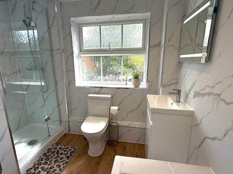 Modern bathroom with walk-in shower, toilet, sink, marble-effect walls and wooden floor
