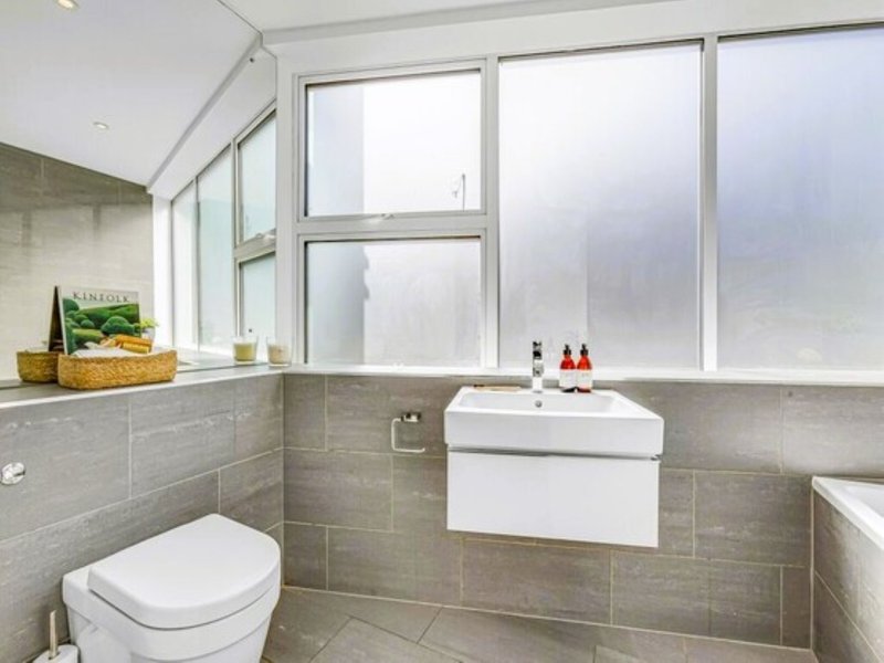 Modern bathroom with toilet, wall-mounted sink, large windows and tiled walls