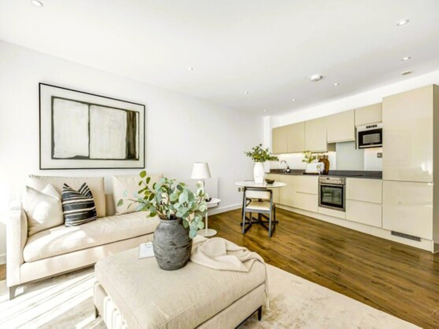 Open-plan living and kitchen space with cream sofa, wooden flooring, and modern fitted kitchen units