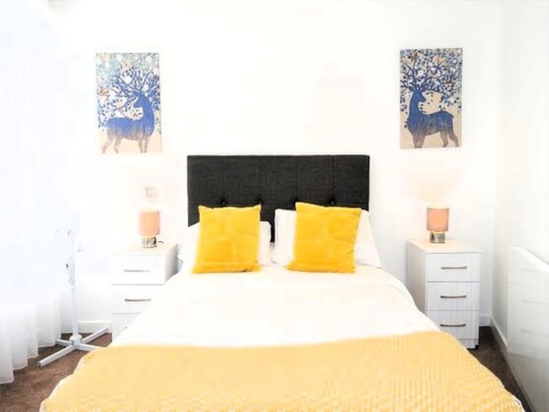 Bedroom with double bed, black headboard, yellow pillows and throw, white nightstands with lamps