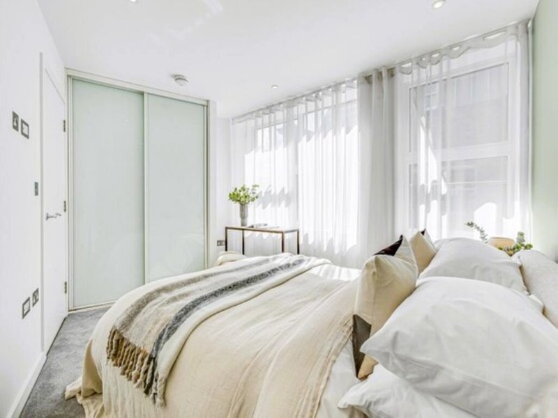 Modern bedroom with double bed, white bedding, pale green wardrobe and sheer curtains
