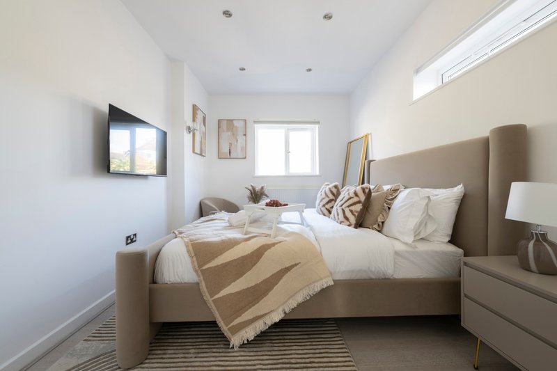 Modern bedroom with grey upholstered bed, white bedding, striped throw, wall-mounted TV and bedside lamps