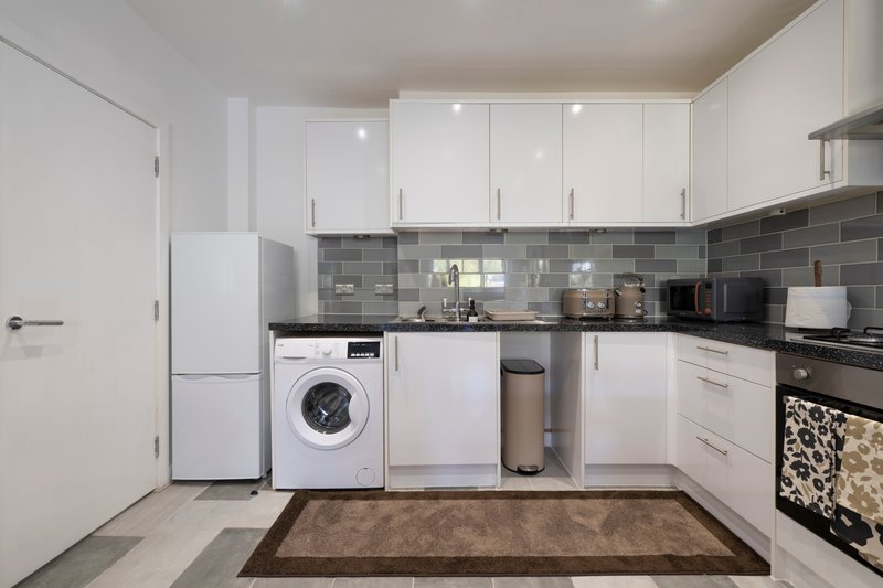 Modern kitchen with white cabinets, gray tile backsplash, washing machine, and stainless steel appliances