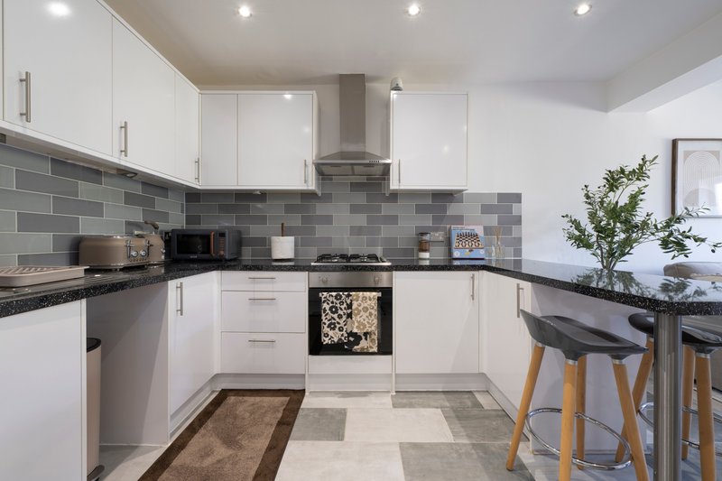 Modern kitchen with white cabinetry, grey tile backsplash, black countertops and breakfast bar seating