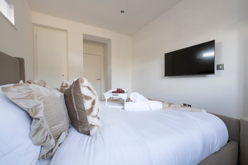 Modern bedroom with double bed, white bedding, decorative pillows and wall-mounted television